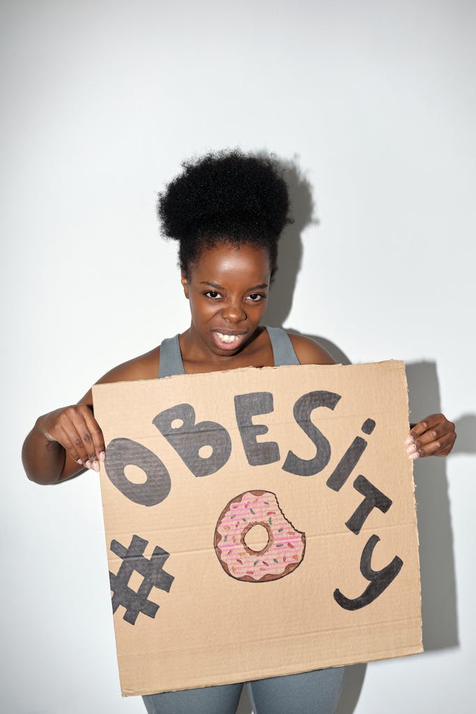 A woman holds a cardboard sign promoting obesity awareness with a colorful design.